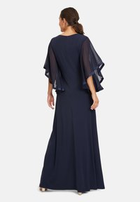 Lång navyblå klänning med genomskinliga vingar, rund halsringning och dragkedja bak. Mjuk tyg med en flödande silhuett.