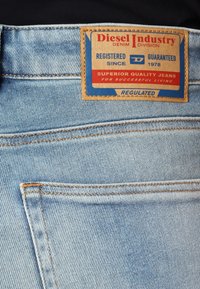 Pantalones vaqueros de denim azul claro con un bolsillo trasero que tiene una etiqueta de cuero marrón de Diesel Industry que dice "Jeans de Calidad Superior" y "Garantizado 1978".