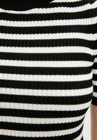 Top en tricot rayé noir et blanc avec une texture côtelée, doté d'un col montant et de manches courtes, présentant des rayures larges et étroites alternées.