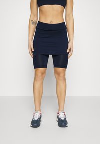 Skort deportivo navy sobre pantalones cortos ajustados, hecho de material elástico. Presenta una cinturilla ancha, textura suave y costuras en contraste.