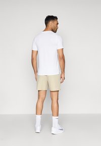 Λευκό κοντομάνικο μπλουζάκι σε συνδυασμό με ανοιχτό μπεζ σορτσάκι, διαθέτοντας κλασική εφαρμογή και απλό σχέδιο. Φοριέται με λευκές κάλτσες και αθλητικά παπούτσια.