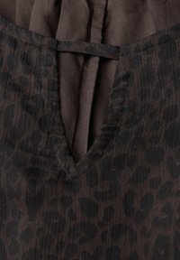 Tessuto marrone con texture che presenta un delicato motivo leopardato nero, con un'apertura a V e un dettaglio di fiocco.