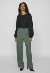 Top negro de mangas largas con mangas abullonadas, combinado con pantalones de pierna ancha verdes de cintura alta, que presentan un cierre de botones y una tela texturizada.