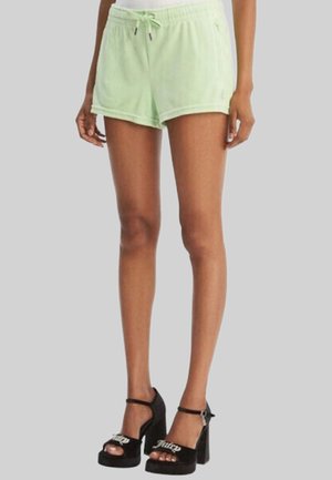 Model draagt lichtgroene badstof short met trekkoord en zwarte plateauhakken met enkelbandjes op grijze achtergrond.