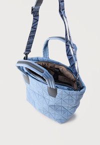 Φωτεινή γαλάζια τσάντα χειρός με δύο κοντές λαβές, έναν μακρύ ρυθμιζόμενο ιμάντα με την ετικέτα "VE" και ένα μερικώς ανοιχτό φερμουάρ που αποκαλύπτει καφέ εσωτερικό.