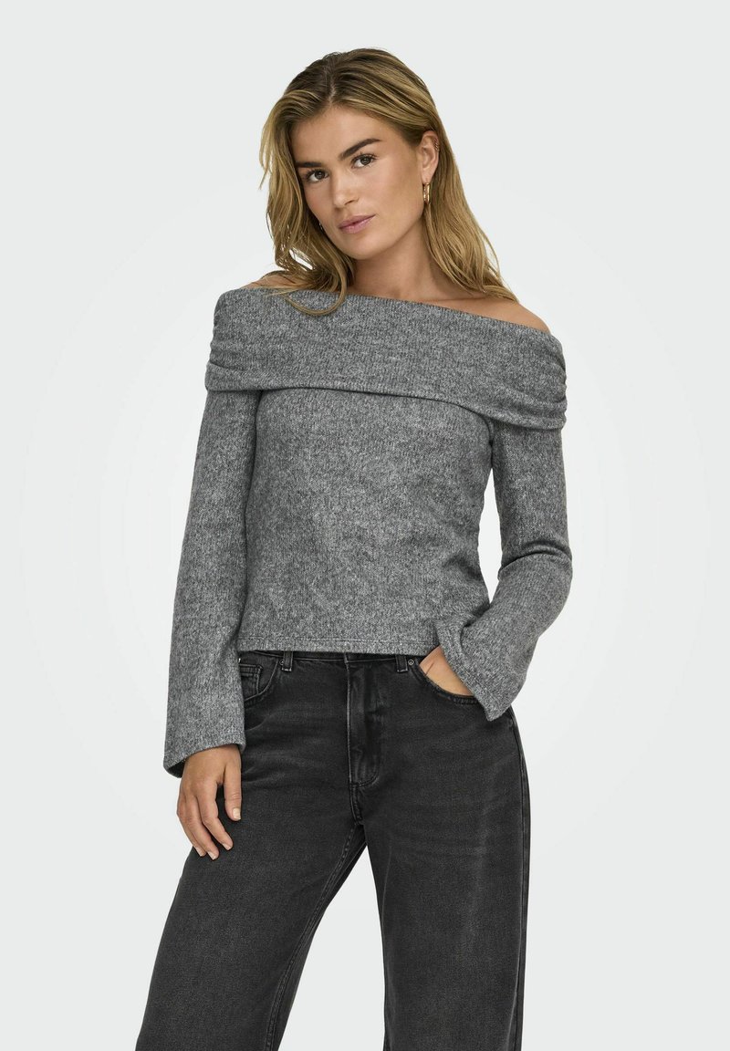 Pull en maille grise, dégageant les épaules, avec une texture douce, des manches longues et un corps cintré. Associé à un jean noir taille haute.