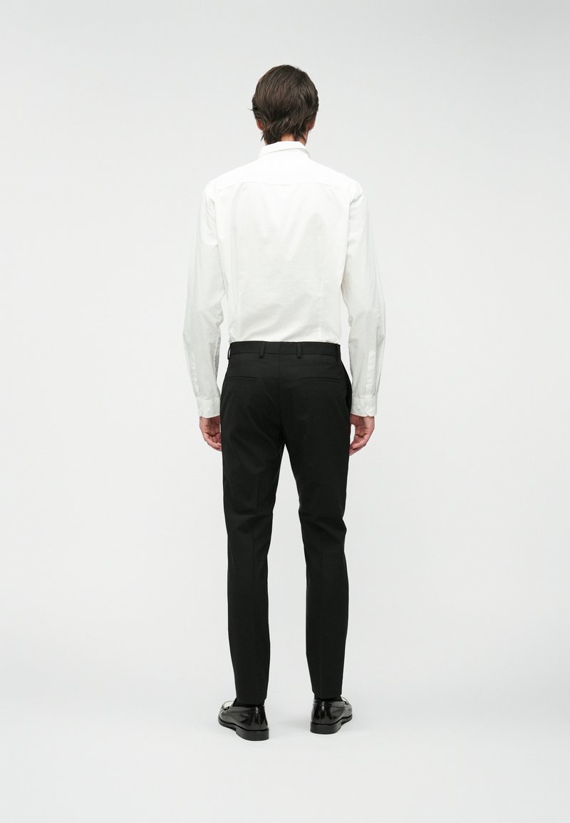 Weißes Langarmhemd mit Button-Down-Kragen, kombiniert mit schwarzen maßgeschneiderten Hosen, von hinten auf einem neutralen Hintergrund präsentiert.