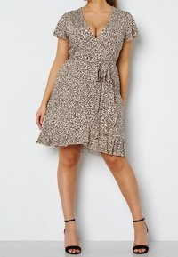 Šaty v béžovém leopardím potisku, s krátkými rukávy a páskem v oblasti pasu, s rozšířeným lemem a volánkovým detailem na spodní části. Černé sandály na vysokém podpatku.