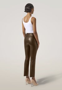 Pantaloni marroni in pelle a vita alta con una vestibilità slim, caratterizzati da cuciture verticali; indossati con un top bianco e scarpe con tacco nudo.