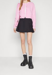Rosa stickad cardigan med rund halsringning och knappstängning, i kombination med en svart plisserad kjol och kraftiga svarta ankelstövlar.