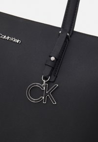 Czarna torebka z faux skóry o strukturalnym kształcie. Posiada srebrny charms z napisem "CK" oraz wytłoczone logo. W komplecie znajduje się długi, regulowany pasek.