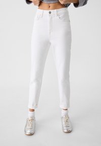 Bílé high-waisted džíny se střihy rovného nohavice, s tradičním pětipocket stylingem a předním zapínáním na knoflík. Rolované manžety Akimbo.