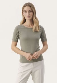 Olivengrøn kortærmet t-shirt lavet af blødt stof med en rund halsudskæring. Sammen med lyse bukser med et enkelt design.