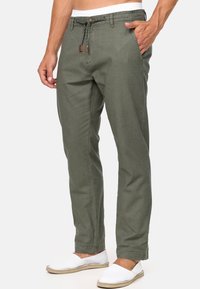 Pantalons chino vert olive avec taille à cordon, poches latérales et coupe slim. Associés à des chaussures blanches sans lacets pour un contraste.