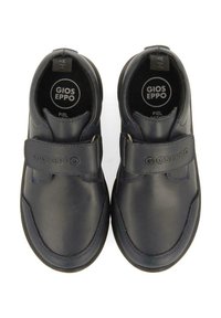 Chaussures en cuir noir avec une finition lisse, une fermeture velcro, un bout arrondi et des accents texturés. Logo de la marque visible sur la surface supérieure.