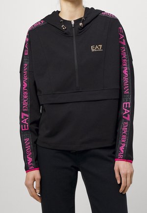 Hoodie noir court avec fermeture éclair à l'avant, bandes avec logo Emporio Armani EA7 rose sur les manches, porté par une personne les mains le long du corps.
