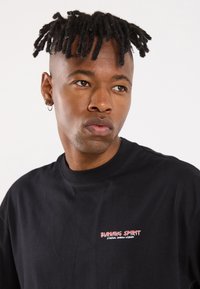 Black t-shirt with short sleeves, round neckline, featuring red and pink text "BURNING SPIRIT" and "ETERNAL SHADOW WISDOM" on the front.