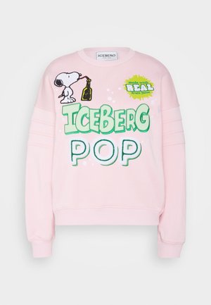 Henkilö, joka pukeutunut vaaleanpunaiseen collegepaitaan, jossa on Snoopy ja teksti "Iceberg Pop", mustiin leggingsseihin, mustiin korkokenkiin ja pitää vaaleansinistä farkkulaukkuja enkelikoristeella.