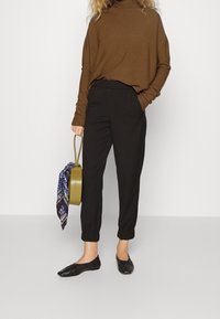 Brązowy, oversize golf, czarne spodnie z elastycznym pasem, czarne baleriny oraz oliwkowa torebka z niebieskim wzorzystym szalem.