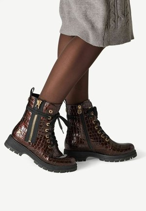 Dark brown croc-patterned leather ankle boots with black laces, side zippers, and gold hardware worn with sheer black tights and a gray knit skirt.