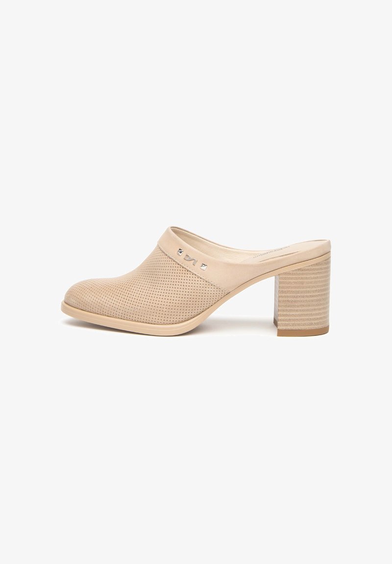 Mule en cuir perforé beige avec un talon bloc et des clous métalliques près du col, présentée de profil sur fond blanc.