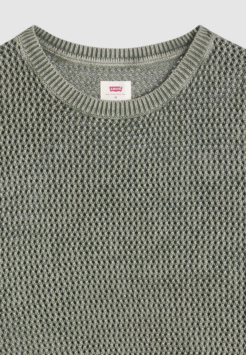 Primer plano de un jersey de punto con textura verde claro, con cuello redondo acanalado y etiqueta visible de Levi's en el interior del cuello.