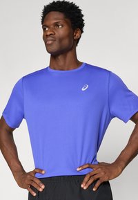 Αθλητικό μπλουζάκι κοντό μανίκι σε ζωηρό μωβ χρώμα, κατασκευασμένο από ελαφρύ ύφασμα, με στρογγυλή λαιμόκοψη και μικρό λευκό λογότυπο στο στήθος.