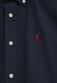 Camicia blu navy con colletto, bottoni bianchi e logo ricamato di un giocatore di polo rosso sul lato sinistro del petto.