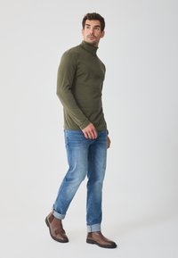 Pulover închis la culoare, cu guler înalt, fit slim; blugi din denim albastru deschis cu ușoară decolorare; cizme din piele maro pentru gleznă, cu panouri elastice pe laterale.