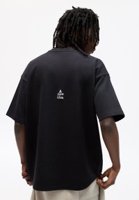 Schwarz oversized T-Shirt mit kurzen Ärmeln, das auf der Rückseite den Text "Eine neue Idee" in Weiß zeigt. Glattes Baumwollmaterial.