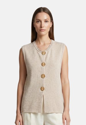 Donna che indossa un gilet beige senza maniche in maglia con quattro grandi bottoni rotondi decorativi sul davanti, abbinato a pantaloni chiari.