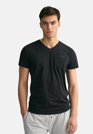 Schwarzes V-Ausschnitt-T-Shirt aus weichem Stoff, mit kurzen Ärmeln und einem kleinen Logo auf der Brust, kombiniert mit grauen Shorts.