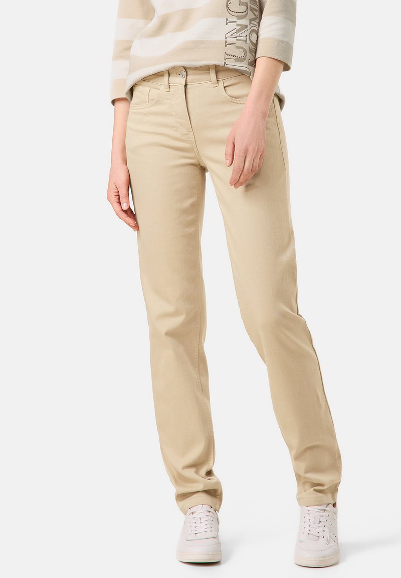 Beige Baumwollhosen mit geradem Schnitt, fünf Taschen und Knopfverschluss. Kombiniert mit einem beige-weißen gestreiften Oberteil und weißen Sneakern.