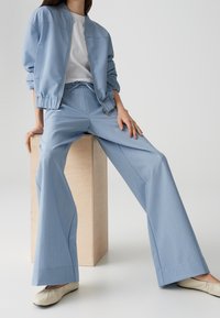 Light blue bomber jacket and matching wide-leg pants in a smooth fabric. White t-shirt underneath, paired with cream ballet flats.