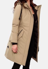 Abrigo acolchado beige con capucha, con cierre de cremallera, bolsillos exteriores y puños acanalados. El interior está forrado con tela oscura.