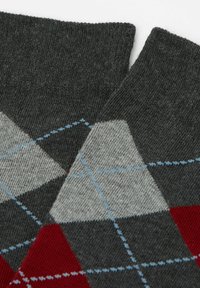 Graue Stricksocken mit einem diamantartigen Argyle-Muster in Rot, Hellgrau und Blau. Der Stoff wirkt weich und strukturiert mit einem gerippten Bündchen.