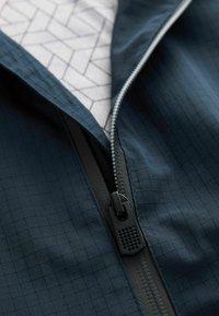 Tessuto della giacca blu navy con motivo a griglia; presenta una cerniera scura e una fodera interna con un design geometrico. Dettagli della superficie testurizzata visibili.