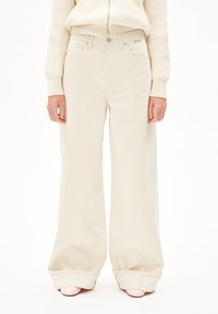 Beige wijde jeans gemaakt van stevige denim, met een hoge taille, voorzakken en een lichte omslag aan de onderkant. Zichtbare gestikte naden.