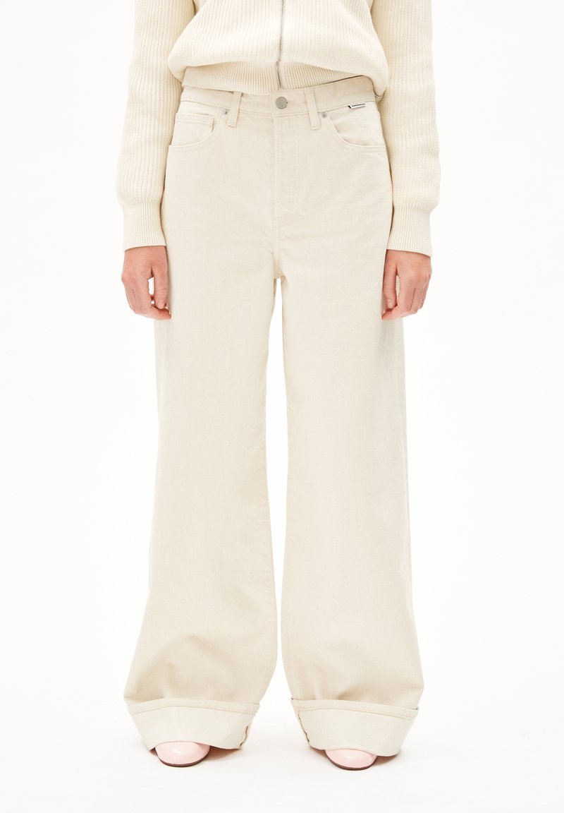 Beige weite Jeans aus robustem Denim, mit hoher Taille, Fronttaschen und einem leichten Umschlag am Saum. Nähte sind sichtbar.