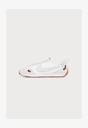 Άσπρο αθλητικό παπούτσι Nike με ανοιχτογκρι σήμα Swoosh, λαστιχένια σόλα και μικρή μαύρη και κόκκινη κεντητή λουλουδένια διακόσμηση στα σημεία της μύτης και της φτέρνας.