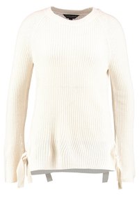 Vit stickad tröja med långa raglanärmar, utrustad med knytband vid sidorna och en texturerad ribbad design. Lätt och avslappnad passform.