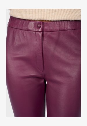 Detailní záběr na vysoké purpurové kožené kalhoty s knoflíkovým zapínáním, nošené s béžovým žebrovaným svetrem zasunutým uvnitř.