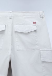 Dos d'un pantalon blanc avec des poches à rabat et un petit écusson du drapeau norvégien au-dessus de la poche droite.