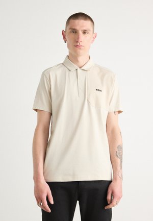 Beige polo skjorte med krave, korte ærmer, en brystlomme og sort "BOSS" logo. Stoffet er glat med et enkelt design.