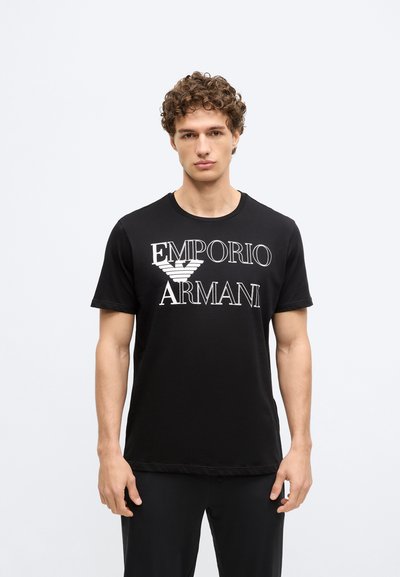 Čierne bavlnené tričko s bielym logom „EMPORIO ARMANI“ a grafikou orla na prednej strane. Klasický okrúhly výstrih a krátke rukávy.