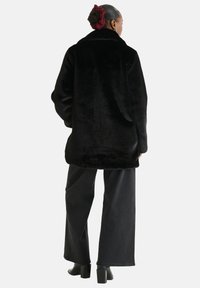 Black faux fur coat with a wide collar, oversized fit, and textured surface, paired with loose black jeans and block-heeled boots.