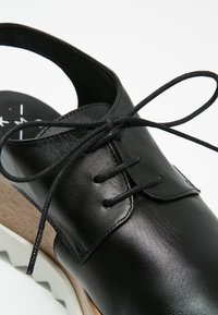 Chaussure en cuir noir avec un dos haut, un laçage à l'avant et un talon en bois léger. Texture lisse et design minimaliste.