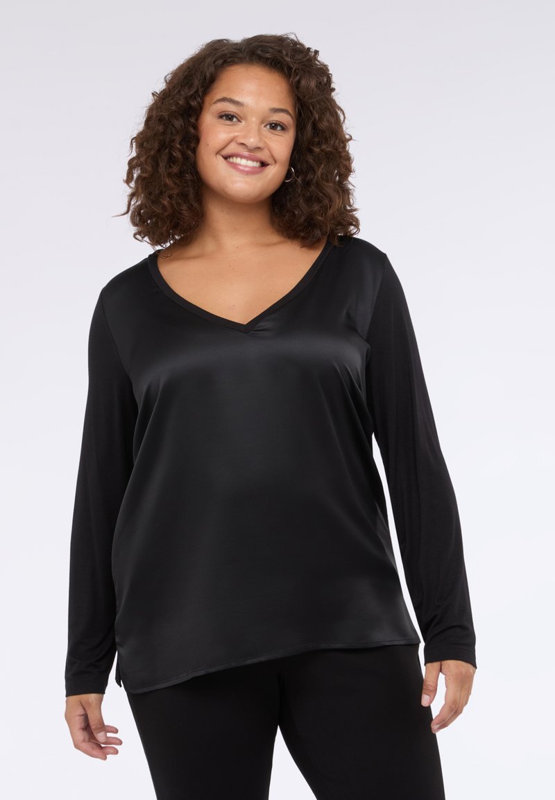 Musta pitkähihainen paita, jossa on V-nuotti, silky-rakenne ja rento istuvuus, jossa on sivuaukot. Yhdistetty mustiin legginsseihin.
