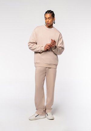 Beige Sweatshirt und passende Hose aus glattem Stoff, mit einem entspannten Schnitt und Rundhalsausschnitt; getragen mit weißen Sneakers.