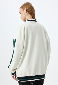 Felpa bianca oversize con polsini e orlo nero e verde a righe. Tessuto morbido, vestibilità rilassata e design minimalista.